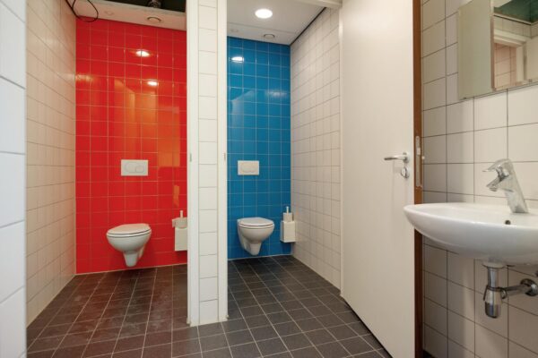 Twee toiletruimtes met felrode en felblauwe wandtegels in een openbaar sanitair op de Harriet Freezerhof.